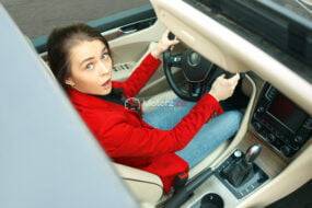 Driving around city. Young attractive woman driving a car. Surprised pretty caucasian model in elegant stylish red jacket sitting at modern vehicle interior. Businesswoman concept. Human emotions concepts