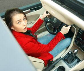 Driving around city. Young attractive woman driving a car. Surprised pretty caucasian model in elegant stylish red jacket sitting at modern vehicle interior. Businesswoman concept. Human emotions concepts